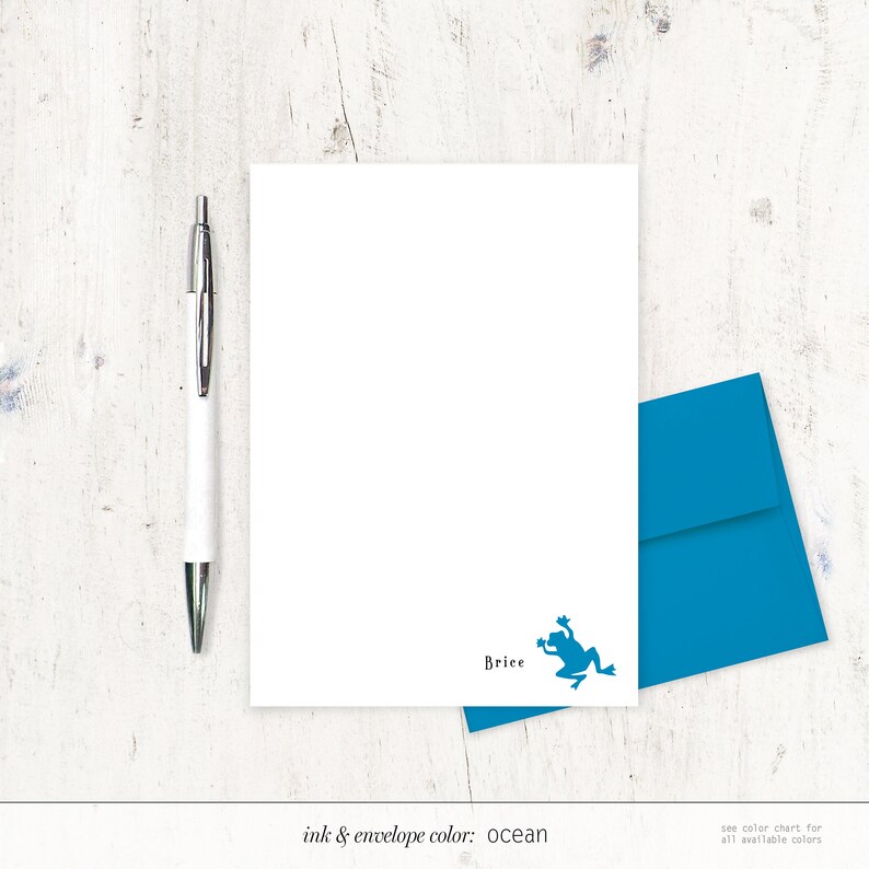 May include: A white stationery set with a blue frog illustration and matching envelope. The set includes a pen and the name "Brice" printed on the stationery. The ink and envelope color is ocean.