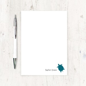 May include: A white notepad with a teal turtle silhouette and the text "Taylor Evans" at the bottom.