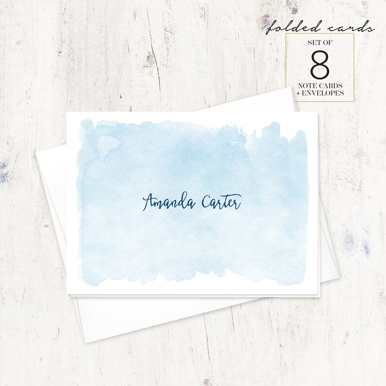 Puede incluir: Un juego de 8 tarjetas plegadas con sobres. Las tarjetas presentan un fondo de acuarela azul claro con el nombre "Amanda Carter" escrito en cursiva azul oscuro.