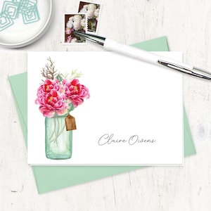 May include: A white card with a watercolor illustration of pink flowers in a mason jar. The card has the name "Claire Owens" written in black cursive.