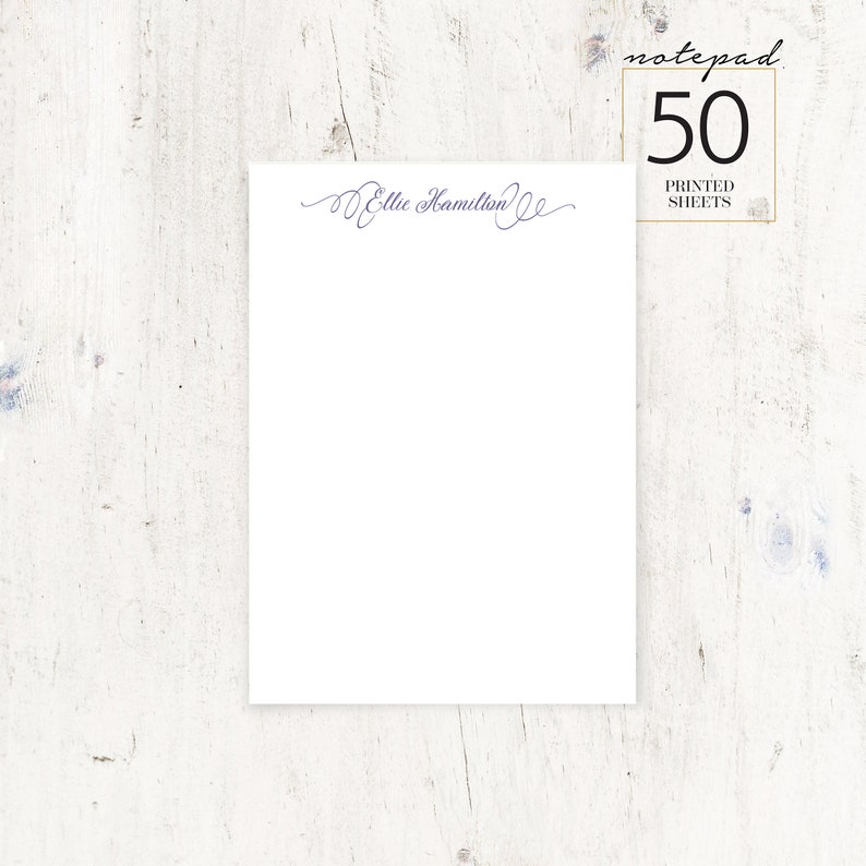 May include: A white notepad with a purple cursive script that says "Ellie Hamilton" at the top. The notepad has a white background and a black border. The notepad is on a white wooden surface. The text "notepad 50 printed sheets" is in a black rectangle in the upper right corner of the image.
