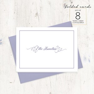 May include: A set of 8 folded note cards with envelopes, featuring a white card with a blue border and the name "Ellie Hamilton" written in cursive script.
