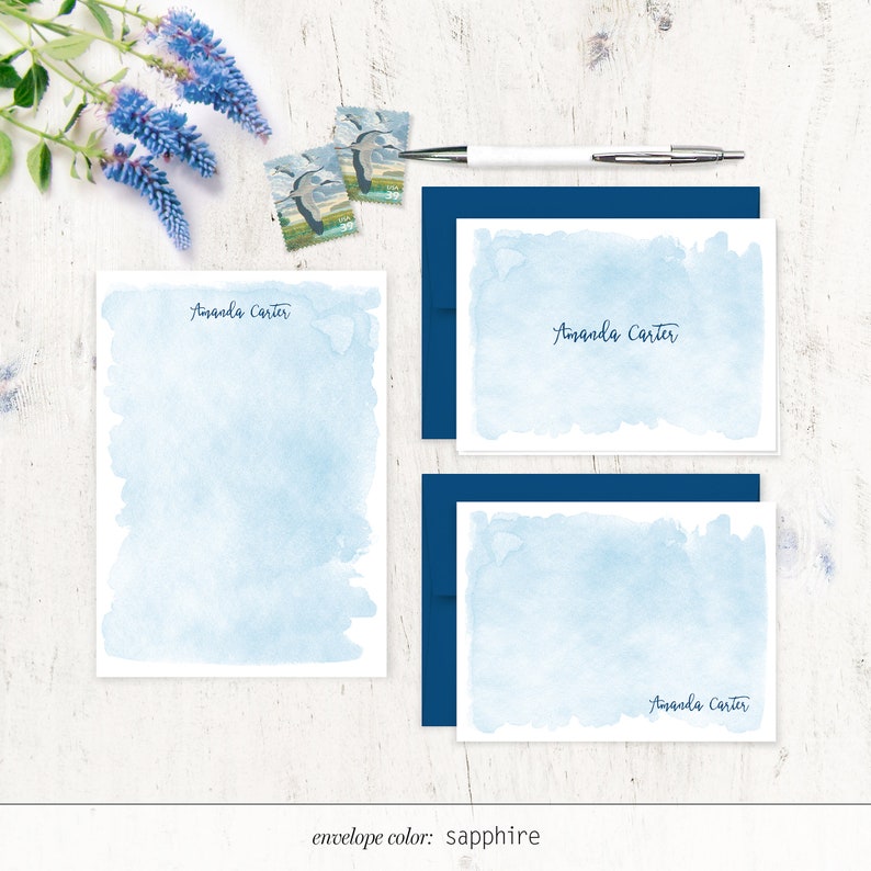 Puede incluir: Un juego de tres tarjetas de papeler&iacute;a de acuarela azul con el nombre "Amanda Carter" impreso en cada tarjeta. Las tarjetas se muestran sobre una superficie de madera blanca con sobres azules y sellos postales. El color del sobre es zafiro.