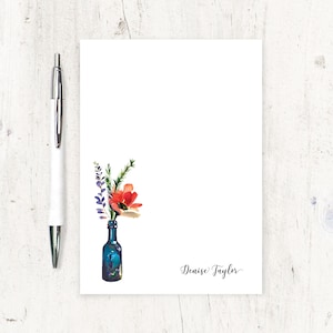 May include: A white notepad with a watercolor illustration of a bouquet of flowers in a blue glass bottle. The name "Denise Taylor" is written in cursive at the bottom of the notepad.