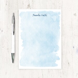 May include: A light blue watercolour notepad with the name "Amanda Carter" written in black ink at the top.