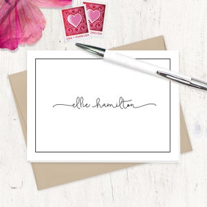 May include: A white card with a black border and the text "ellie hamilton" written in cursive script.