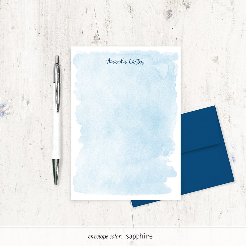 May include: A light blue watercolour stationery set with the name "Amanda Carter" printed at the top. The set includes a sheet of stationery and a sapphire blue envelope.