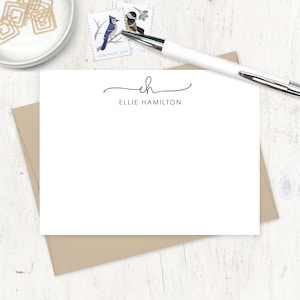 May include: White stationery card with a black cursive monogram "eh" and the text "Ellie Hamilton" below it.