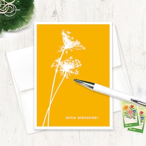 May include: A yellow card with a white silhouette of two Queen Anne's Lace flowers. The text "anne alexander" is printed at the bottom of the card.