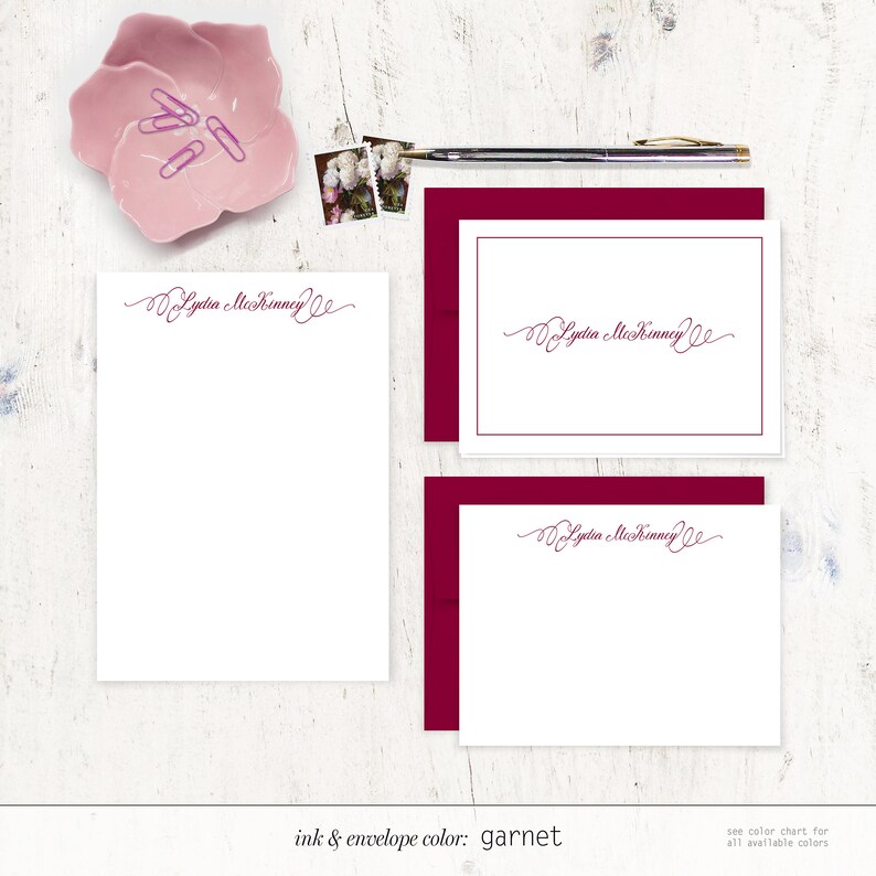 May include: A set of three white stationery cards with a burgundy envelope. The cards feature a handwritten script font with the name "Lydia McKinney" in a burgundy ink color. The text "ink & envelope color: garnet" is printed at the bottom of the image.
