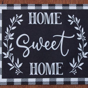May include: Black and white checkered doormat with the text "Home Sweet Home" in white lettering with a white floral design on each side.