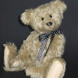 May include: A light brown teddy bear with black and white polka dot ribbon around its neck. The bear is sitting on a black background.
