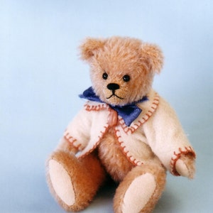 May include: A light brown teddy bear wearing a white jacket with red stitching and a blue bow tie. The bear is sitting on a light blue background.