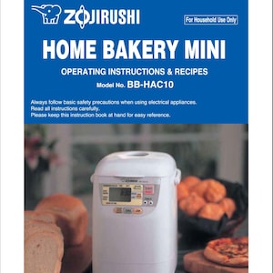 May include: A white Zojirushi Home Bakery Mini bread maker with a digital display showing 3:30. The bread maker has buttons for cake, jam, and timer. The bread maker is on a countertop with a loaf of bread and a basket of rolls in the background.