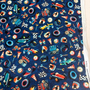 May include: Dark blue fabric with a repeating pattern of race cars, tires, helmets, wrenches, flags, and stopwatches. The cars are red, yellow, and blue. The tires are black and blue. The helmets are orange, white, and blue. The wrenches are silver.