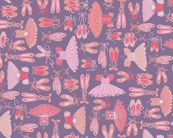 May include: A purple fabric featuring a repeating pattern of pink ballet tutus and pairs of ballet slippers with ribbons. A white ruler is visible at the bottom edge, showing measurements in inches from zero to seven inches across the fabric.