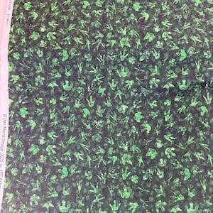 May include: Green and black fabric featuring a pattern of dinosaur footprints. The footprints are in various sizes and orientations, creating a textured, all-over design. The fabric has a mottled appearance, with darker and lighter shades of green.