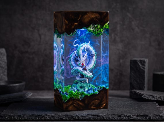 A hand-sculpted white dragon coiled inside a glowing epoxy resin diorama — functional lamp meets fantasy tabletop art.