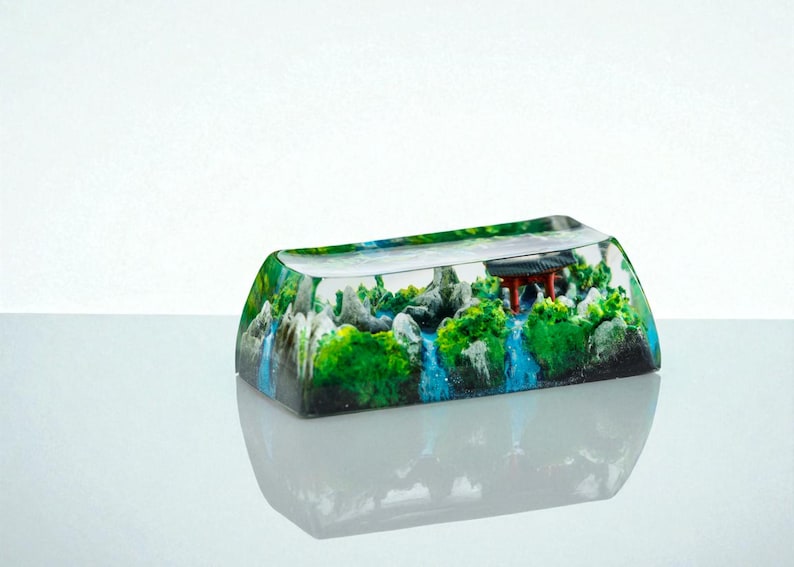 Puede incluir: Una tecla rectangular de resina transparente con una escena de paisaje en miniatura. La escena incluye una pagoda roja, follaje verde, cascadas y rocas grises. La tecla est&aacute; dise&ntilde;ada para un teclado mec&aacute;nico.