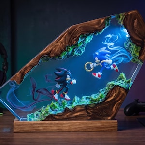 May include: A decorative resin and wood lamp featuring Sonic the Hedgehog and Shadow the Hedgehog figures suspended in a blue-lit environment. The scene includes green textured terrain, flowing blue light effects, and a gold ring.