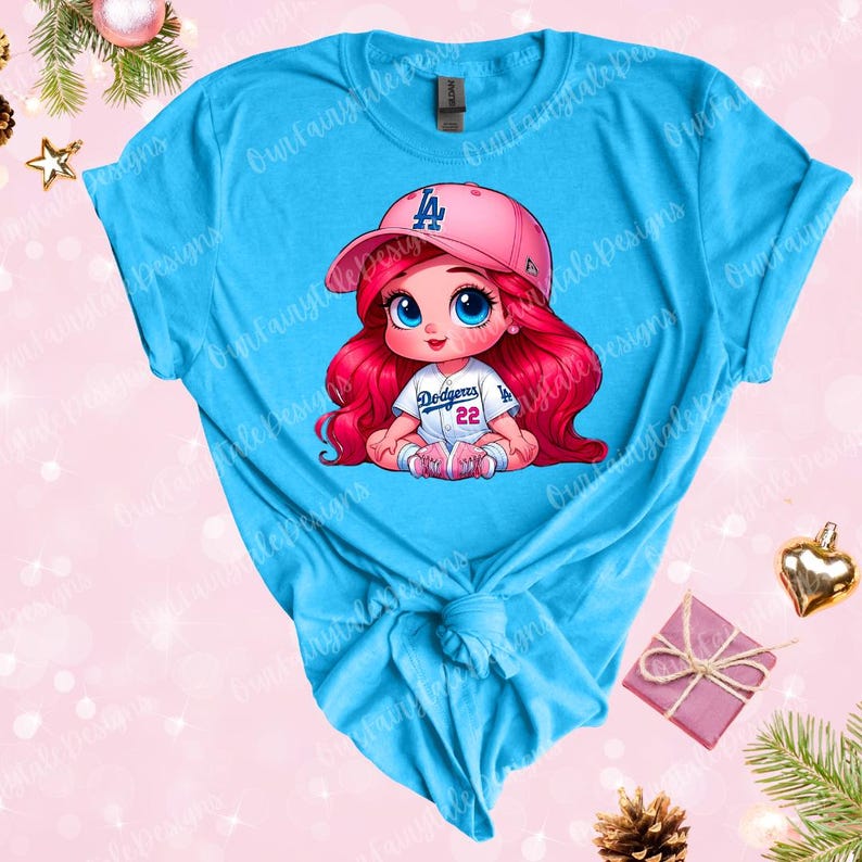 May include: A turquoise t-shirt with a cartoon image of a girl wearing a pink baseball cap with the letter "L" on it. The girl is wearing a white baseball jersey with the words "Dodgers" and the number "22" on it. She has long red hair and blue eyes.