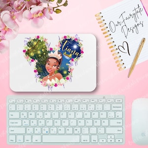 May include: A white mouse pad with a cartoon image of Tiana from Disney's Princess and the Frog. The image is surrounded by flowers and vines. The text "Tiana" is written in a whimsical font above the image.