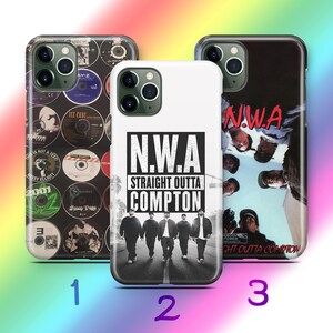Peut inclure: Trois étuis de téléphone différents représentant une image en noir et blanc d'un groupe d'hommes marchant dans la rue avec le texte "N.W.A. Straight Outta Compton". Le premier étui présente un collage de pochettes d'album, le deuxième étui présente l'image de N.W.A. et le troisième étui présente une image en noir et blanc d'un groupe d'hommes avec le texte "N.W.A."