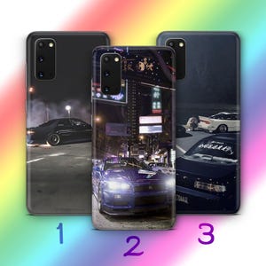 Könnte beinhalten: Drei verschiedene Handyhüllen-Designs mit einem schwarzen Auto, einem blauen Auto und einem weißen Auto. Die Designs sind alle vor einem nächtlichen Stadtbild.