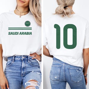A woman wearing a white t-shirt with the text "SAUDI ARABIA" printed on it, along with the number "10" on the back.
