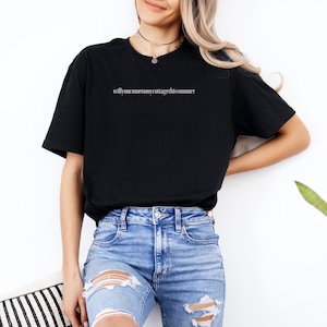 May include: Black t-shirt with the text "willyoucometomyvintagechissummer" in a minimalist font. The shirt is paired with light blue ripped jeans. A casual, everyday outfit.