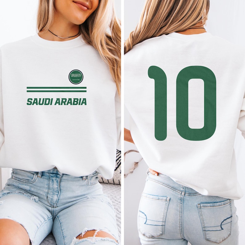 A woman wearing a white sweatshirt with the text "SAUDI ARABIA" printed on it, along with a green number 10.