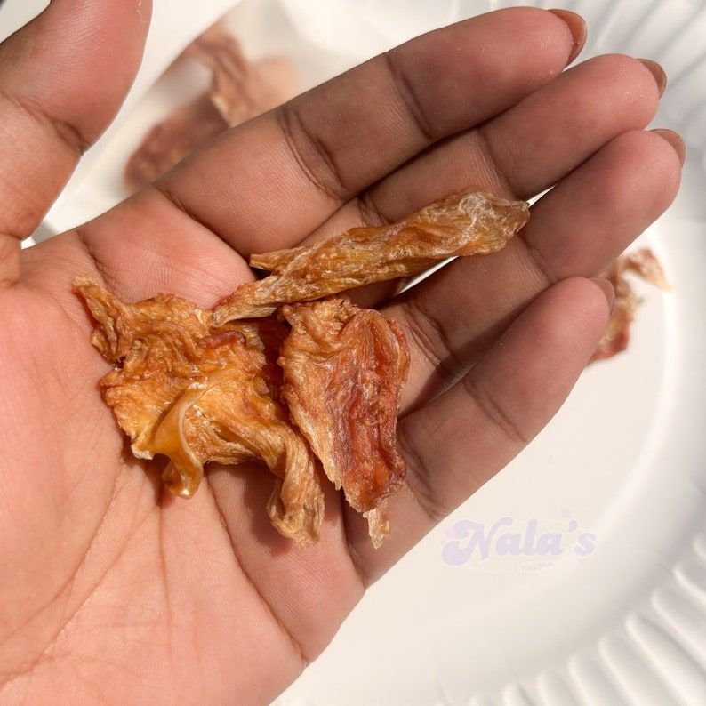 Pu&ograve; includere: Primo piano di una mano che tiene diversi pezzi di pollo essiccato. Il jerky &egrave; di colore marrone chiaro e ha una tonalit&agrave; leggermente rossastra. Il jerky &egrave; disposto in un mucchio nel palmo della mano.