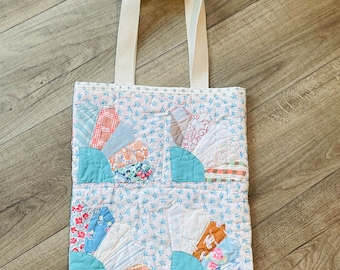 Könnte beinhalten: Eine Patchwork-Tragetasche mit einem weißen Canvas-Trageriemen. Die Tasche ist aus verschiedenen Stoffen in Blautönen, Rosa und Braun gefertigt. Der Stoff ist gesteppt und hat ein Blumenmuster.