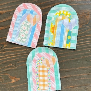 May include: Three fabric appliques in an arch shape, featuring rainbow designs. Each has a heart and uses patterned fabrics like stripes and gingham. The colours include pink, blue, green, yellow, and orange. Measurements are in centimetres.