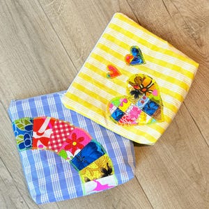 Peut inclure: Deux pochettes en tissu avec des motifs de cœurs en patchwork. Une pochette est jaune avec des rayures blanches et l'autre est bleue avec des rayures blanches. Les deux pochettes ont des cœurs en patchwork colorés.