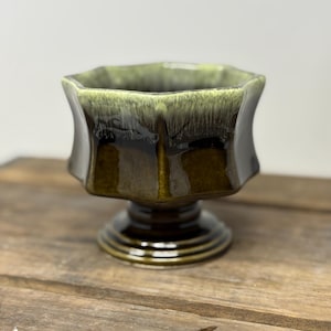 以下が含まれることがあります： 八角形の縁が付いた、ヴィンテージスタイルの陶器製ボウル。ボウルは、内側が淡い緑色、外側が濃い茶色というツートンカラーの釉薬が施されています。丸みを帯びた段付きの台座に置かれ、レトロな美学を表現しています。
