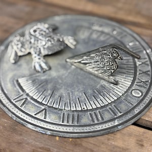 以下が含まれることがあります： ローマ数字と鳥の形をした指針が付いた、風化した円形のサンダイヤル。 サンダイヤルは、使い古した仕上げの金属素材で作られており、詳細な鳥とフクロウのデザインが特徴です。 装飾的な庭のアクセント。