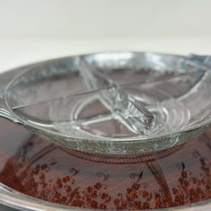 Puede incluir: Un juego de servir vintage con un plato de vidrio transparente dividido con borde plateado, sobre una bandeja con borde plateado y base marrón oscuro con estampado floral. Ideal para aperitivos.