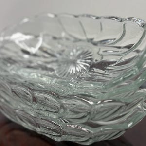 May include: A stack of clear glass dishes with a leaf-like design. The dishes have a scalloped edge and a textured surface. The glass is transparent, allowing light to pass through. The dishes are likely for serving food.
