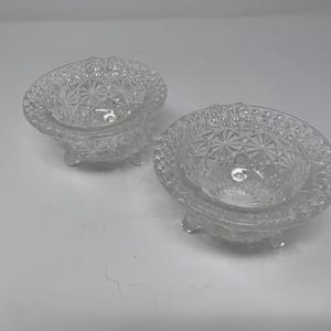 May include: Two clear glass footed bowls with a diamond pattern. The bowls are empty and have a slight shine.