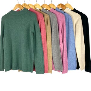 May include: A selection of long-sleeved jumpers in a range of colours, including green, pink, tan, grey, purple, blue, beige, and black, displayed on wooden hangers. Each jumper features a mock neck and a classic design.