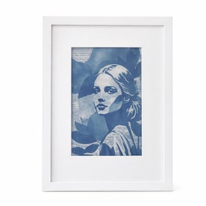 Puede incluir: Una impresión artística enmarcada que presenta un retrato en tonos azules de una mujer con elementos florales y textuales. La obra de arte está en un marco blanco, creando una estética limpia y moderna. La paleta de colores de la impresión es principalmente azul y blanco.