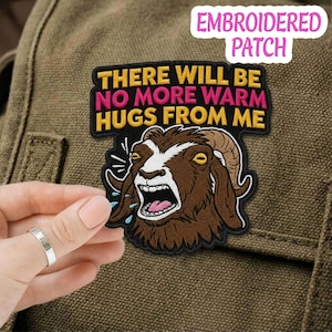 Può includere: Toppa ricamata con un'illustrazione di capra marrone, con la bocca aperta e gli occhi gialli. La toppa recita "THERE WILL BE NO MORE WARM HUGS FROM ME" in giallo e rosa. Sfondo nero con bordo giallo.