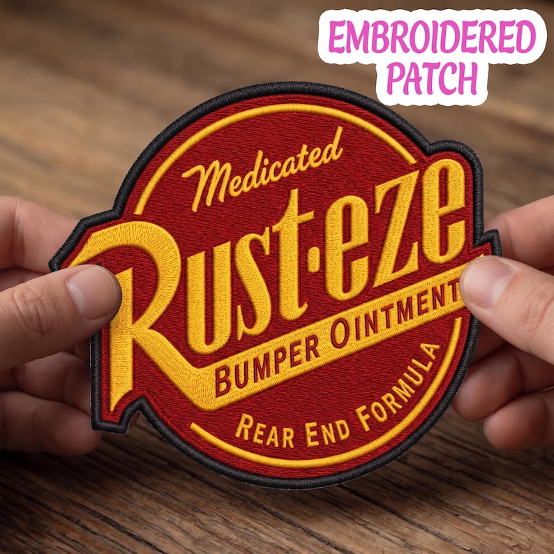 May include: A circular embroidered patch featuring a deep red background with a black border. The text reads Medicated Rust-eze BUMPER OINTMENT REAR END FORMULA in bold yellow lettering. The design is stylized with a prominent yellow R.