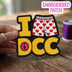May include: Embroidered patch with the text "I DCC" in yellow, black, and white. The "I" is a yellow letter, and the "DCC" has a pink eye design. The patch features a pair of white underwear with red hearts.