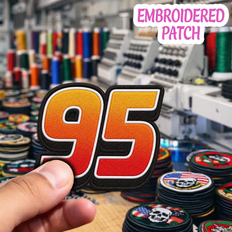 May include: An embroidered patch featuring the number 95 in a bold, block font. The digits display a vibrant gradient transition from yellow at the top to orange and red at the bottom, all outlined with a thick black border and white trim.