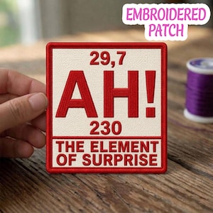 May include: Embroidered patch with a red border and a cream-colored center. Bold red text reads "AH!" with the numbers "29,7" and "230". The phrase "THE ELEMENT OF SURPRISE" is below. A purple spool of thread is in the background.