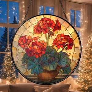 May include: A round stained glass window panel featuring a floral design. The artwork depicts a pot of red geraniums with green leaves against a yellow and brown background. The panel is framed in black and hangs from a chain.