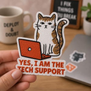 May include: An embroidered patch featuring a white and brown tabby cat sitting behind an orange laptop. The patch includes the orange text "YES, I AM THE TECH SUPPORT" at the bottom. The design has a white border and a detailed stitched texture.