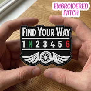 May include: A black embroidered patch featuring the white text FIND YOUR WAY above a motorcycle gear shift pattern of 1, N, 2, 3, 4, 5, 6. The N is green, the 6 is red, and the design includes white wings flanking a central motorcycle wheel.